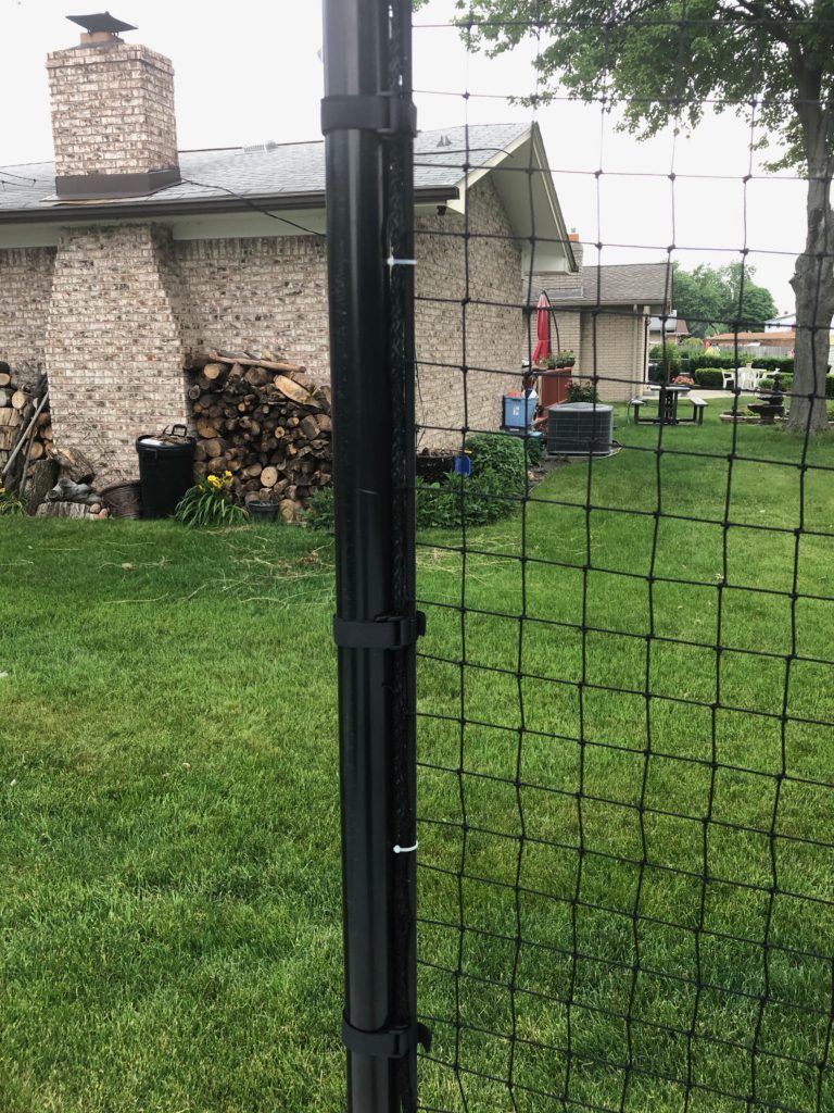 Nylon Netting Panels Strapped to Posts at a Home Basketball Hoop Area